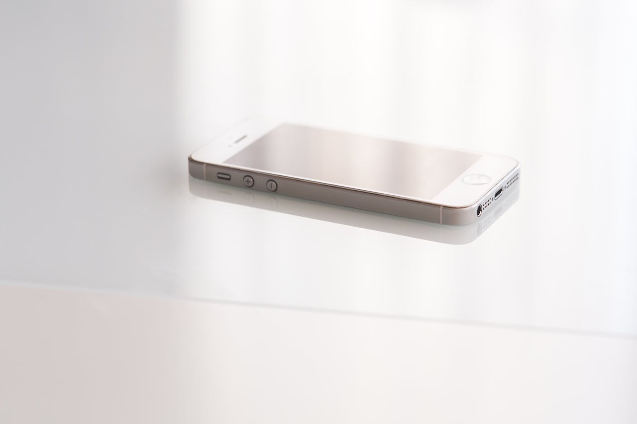 A sleek white smartphone placed on a reflective surface ideal for modern tech concepts.